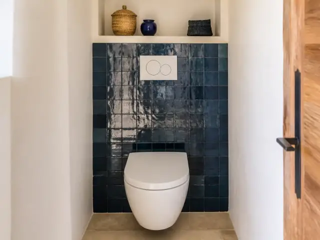 Toilettes avec un WC suspendu devant un mur de zellige bleu nuit brillant, murs latéraux peints en blanc cassé