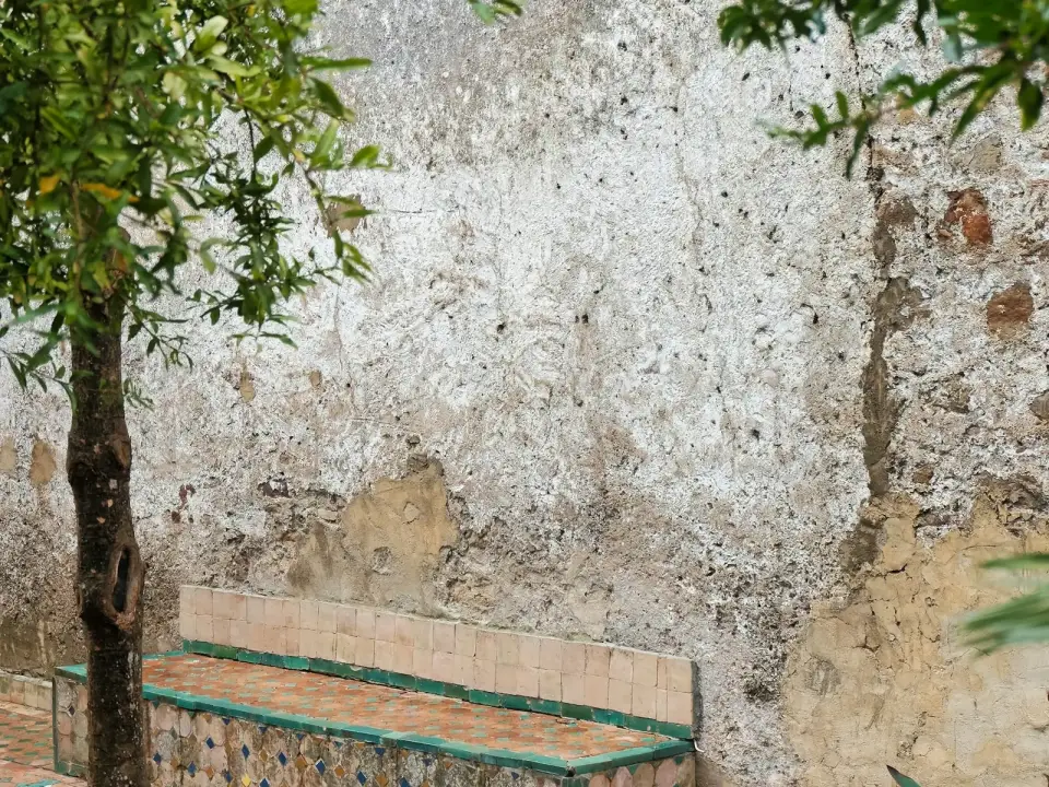 Banc carrelé de zellige contre un mur de pierre patiné, à l’ombre d’un arbre