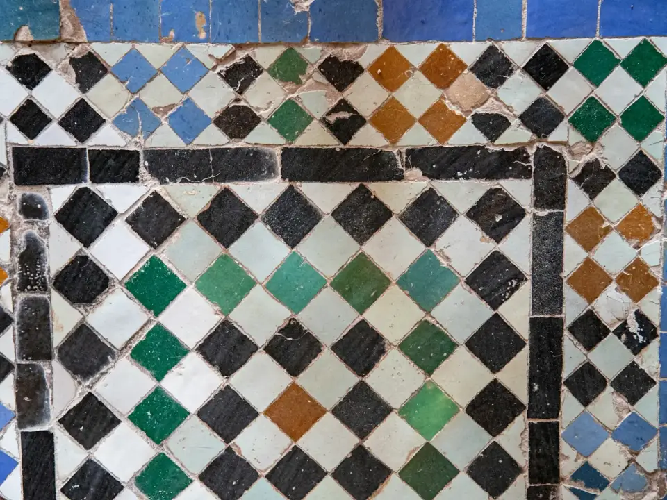 Gros plan sur des carreaux de zellige vert émaillés, aux bords taillés irréguliers et aux reflets inégaux