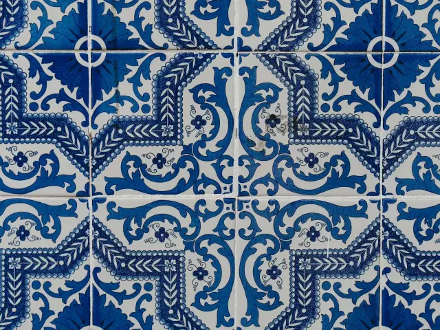 Façade couverte d’azulejos bleus et blancs à motifs floraux à côté d’un panneau de zellige géométrique vert