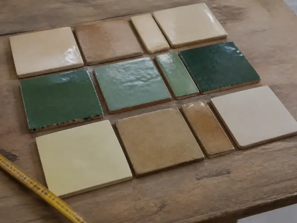 Carreaux de zellige carrés et rectangulaires de plusieurs couleurs alignés sur un établi à côté d’un mètre ruban