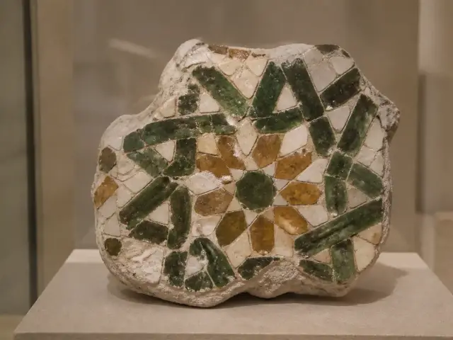 Fragment ancien de zellige à motif géométrique vert et brun exposé dans une vitrine de musée