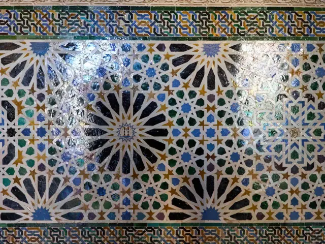 Panneau de mosaïque géométrique en faïence taillée, étoiles et entrelacs verts, bleus et ocre sur un mur ancien
